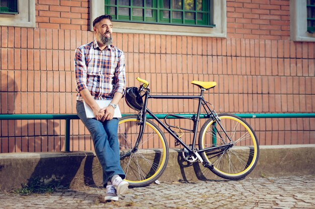 Улыбающийся случайный бизнесмен с перерывом. Он стоит перед зданием рядом с велосипедом и держит ноутбук.