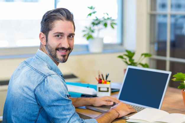 Uomo d'affari casuale sorridente che scrive sul computer portatile