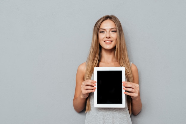 Photo smiling casual woman showing blank tablet computer screen isolated on a gray background