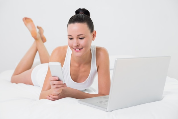 Smiling casual woman using cellphone in bed