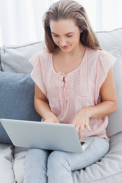 Smiling casual woman using laptop on sofa