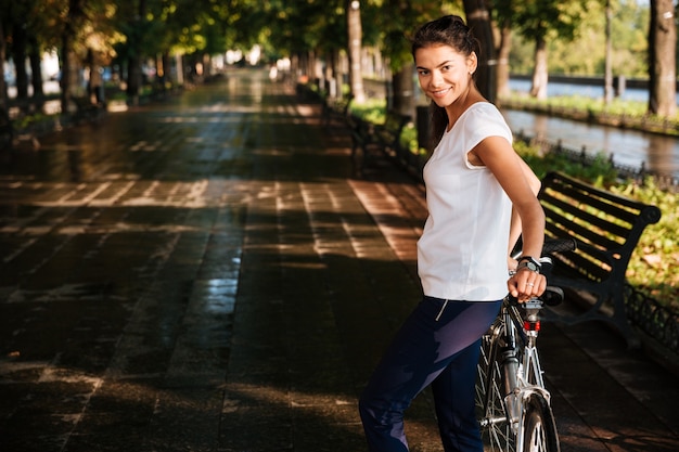 Sorridente donna casual con la bicicletta nel parco strada