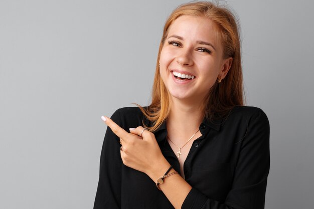 Smiling casual young woman pointing finger at copy space