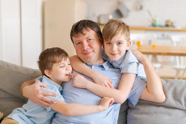 Smiling caucasian dad cheerfully plays with cute little sons on sofa at home in living room against ...