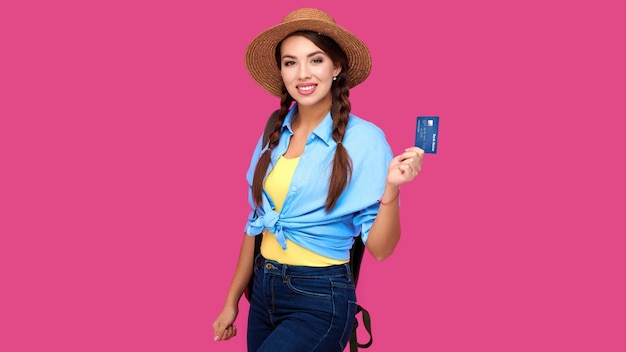 선명한 분홍색 외진 배경에 신용카드를 들고 웃고 있는 백인 여학생, 배낭을 메고 여행하는 젊은 여성