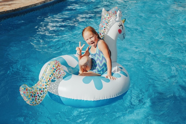Smiling caucasian girl lying on inflatable ring unicorn kid child having fun in swimming pool