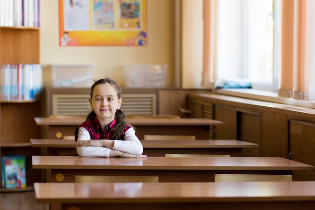 Улыбающаяся девушка кавказской, сидя за столом в классной комнате