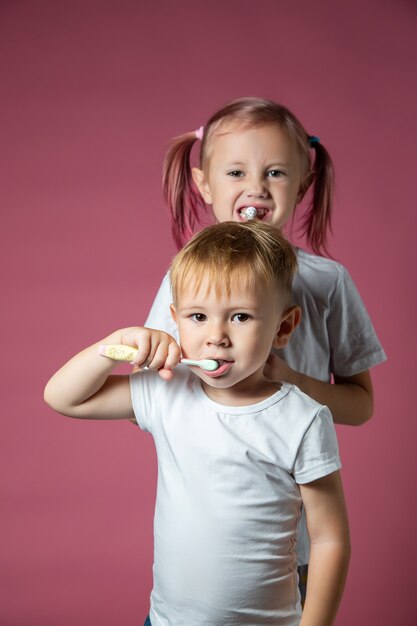 ピンクの背景に電気ソニックと手動歯ブラシで彼の歯を掃除している白人の小さな男の子と女の子の笑顔。