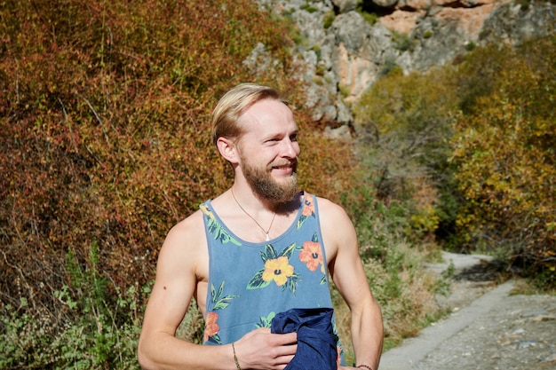 A smiling Caucasian male in a colorful shirt walking in the forest on a sunny day