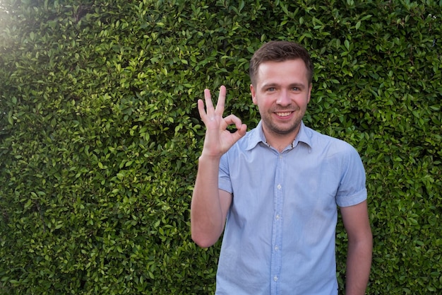 A smiling caucasian man showing ok sign on green eco grass