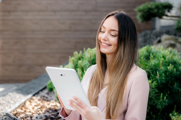 Photo smiling caucasian office employee looking at tablet screen and sitting outdoors