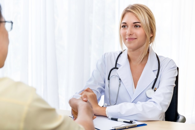 Smiling Caucasian woman confident doctor shaking hands with senior Asian patient in the hospital room.