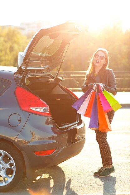 Photo smiling caucasian woman putting her shopping bags into the car trunk