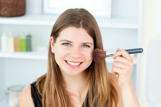 Smiling caucasian woman putting powder on her face smiling at th