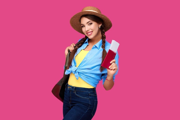 Smiling caucasian woman student holding passport and plane tickets Girl in casual clothes and straw hat Female traveler on pink isolated background