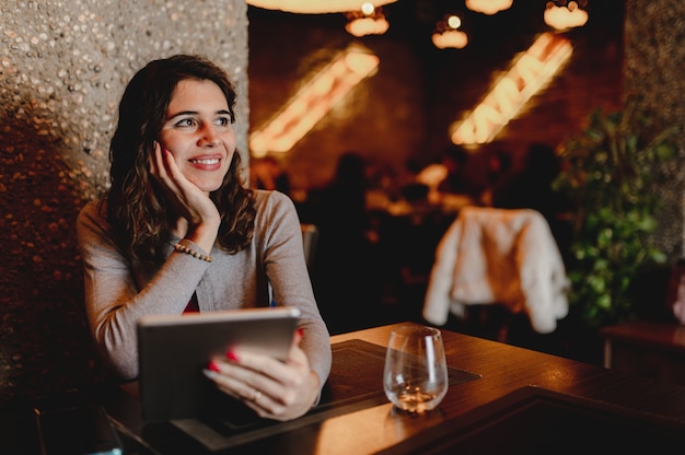 Улыбающаяся кавказская молодая женщина в ресторане с планшетом