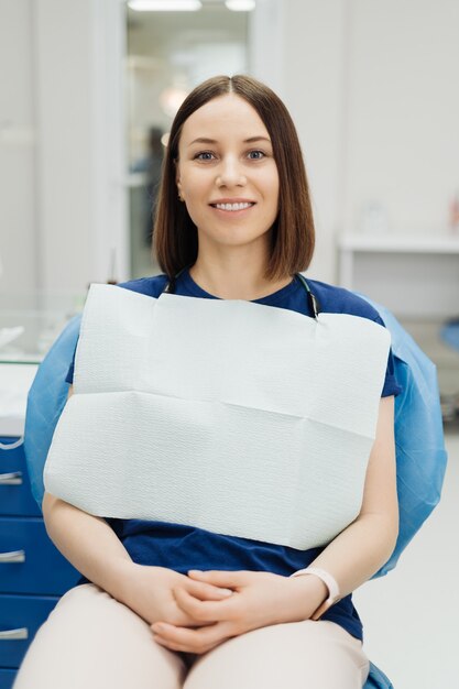 Foto sorridente giovane donna caucasica paziente al controllo sanitario del dentista seduto su una sedia di stomatologia guardando davanti