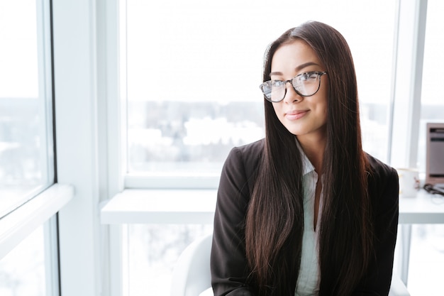 Smiling charming asian young businesswoman standing near the window