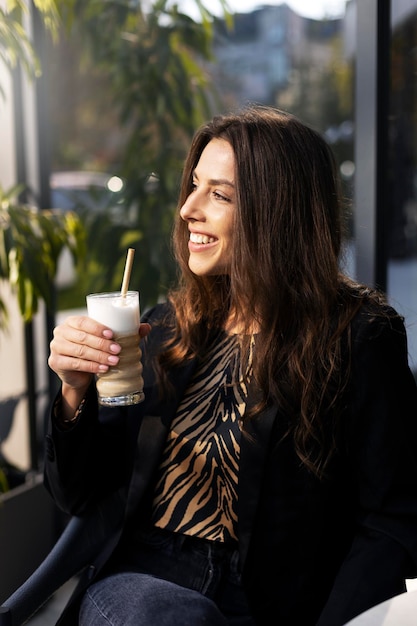 Smiling charming woman holding a drink in her hand smiling and looking away on the street A dreamy girl during a lunch break