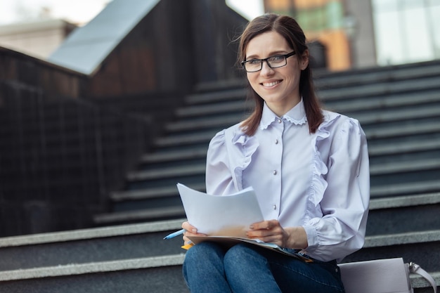 Smiling cheerful caucasian business woman with glasses sitting on stairs