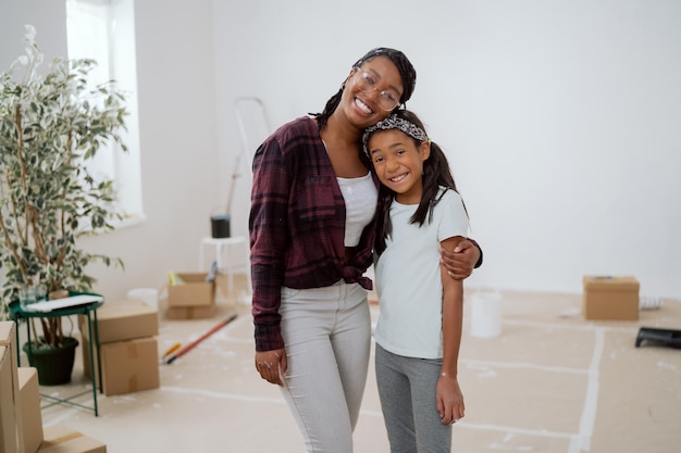 Smiling cheerful woman with glasses in homemade clothes embraces her school age daughter