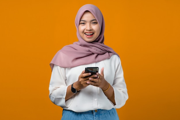 Smiling and cheerful young asian woman using mobile phone on yellow