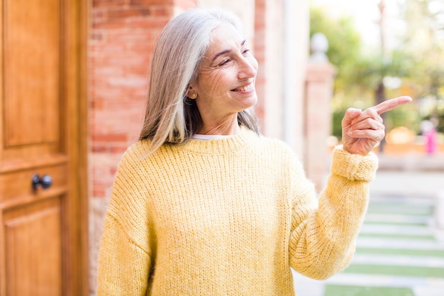 Smiling cheerfully feeling happy and pointing to the side and upwards showing object in copy space