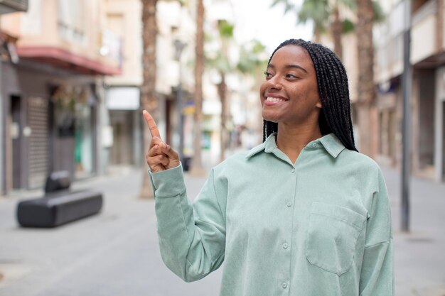 Smiling cheerfully feeling happy and pointing to the side and upwards showing object in copy space