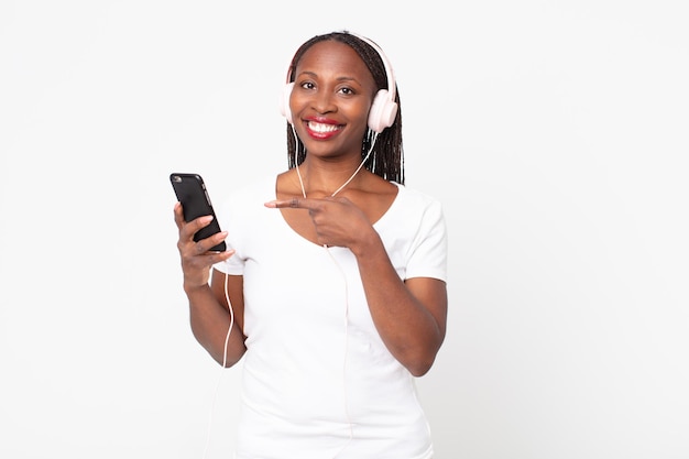 Smiling cheerfully, feeling happy and pointing to the side with headphones and a smart phone