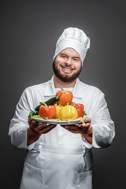 Smiling chef showing plate with vegetables