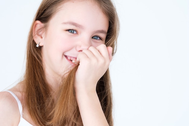 smiling child covering her mouth and teeth with hair on white wall.