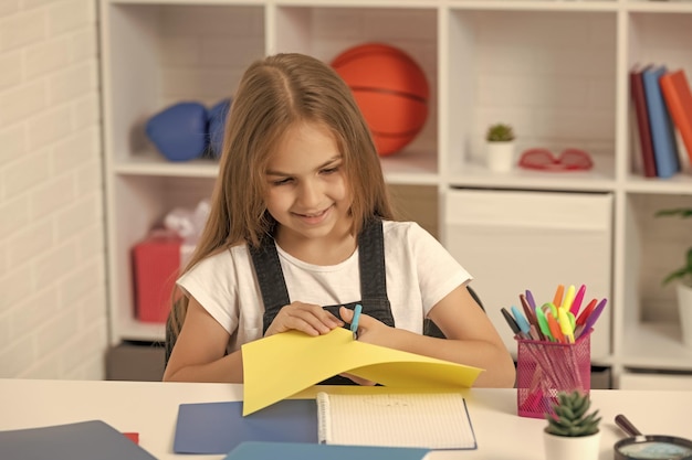 Smiling child cut paper in school classroom