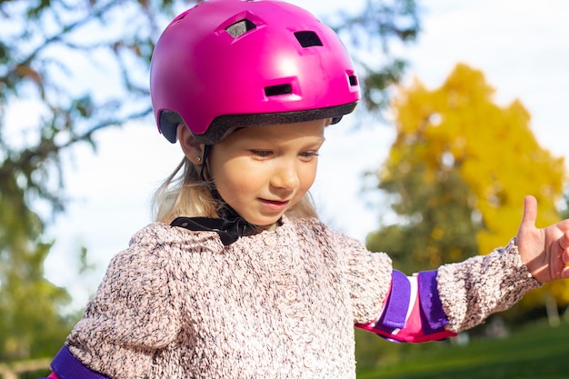 Photo smiling child girl in a helmet in protection rollerblades in the park