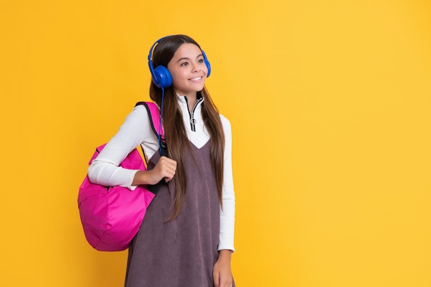 Улыбающийся ребенок в наушниках со школьным рюкзаком на желтом фоне