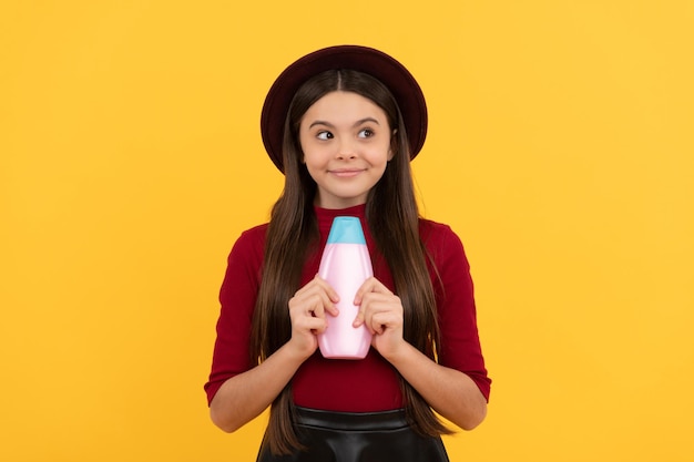 Smiling child hold shampoo bottle on yellow background daily habits