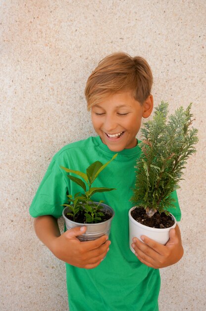 Photo smiling child holding green plant in pot grey background