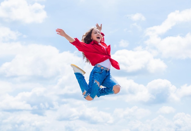 Фото Улыбающийся ребенок прыгает так высоко беззаботно и радостно в стиле детской моды девочка-подросток на фоне неба открытый хипстерский ребенок прыгает счастливый детский день счастливое детство уверенная и стильная красота