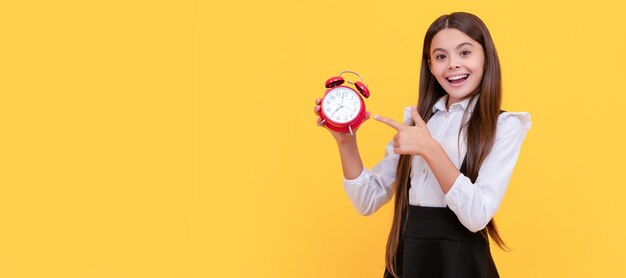 Smiling child in school uniform point finger on alarm clock showing time back to school teenager child with clock alarm horizontal poster banner header copy space