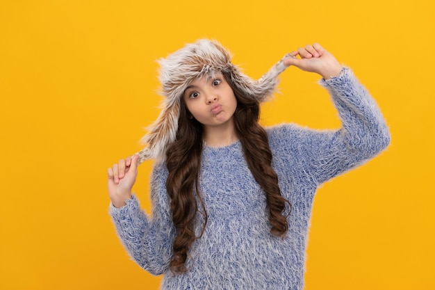 Smiling child in sweater and earflap hat on yellow background wintertime