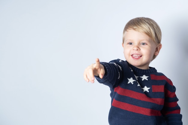 Smiling child in a sweater with an American USA flag is pointing at something on a white background