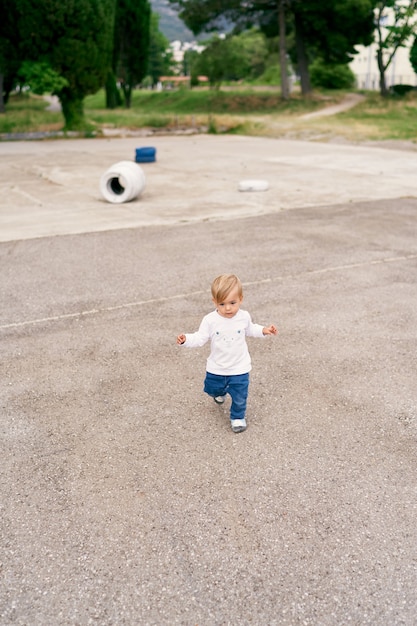 Фото Улыбающийся ребенок гуляет по бетонной детской площадке на фоне автомобильных шин