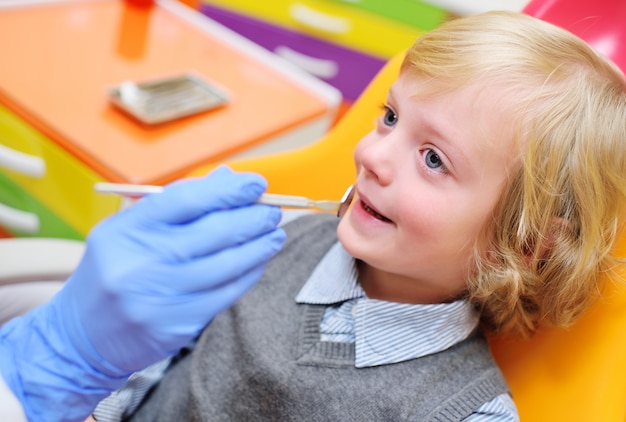 Bambino sorridente con capelli ricci leggeri su esame nella sedia dentale