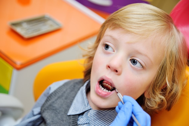 Foto bambino sorridente con capelli ricci chiari su esame nella sedia dentaria