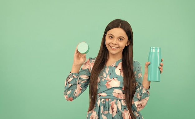 Smiling child with long hair hold shampoo and face cream beauty