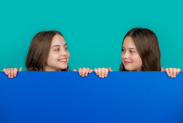 Smiling children behind blank blue paper with copy space for advertisement