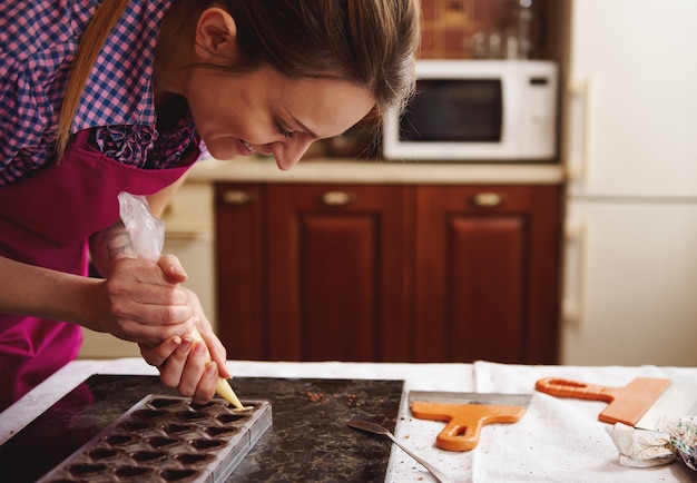 Улыбающийся шоколатье наслаждается приготовлением роскошных шоколадных конфет ручной работы на домашней кухне к празднованию всемирного дня шоколада