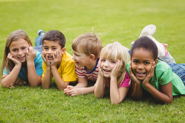 Smiling classmates lying in a row in grass