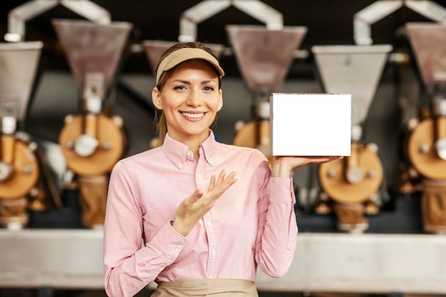 A smiling coffee factory worker holding a box with coffee and pointing at it