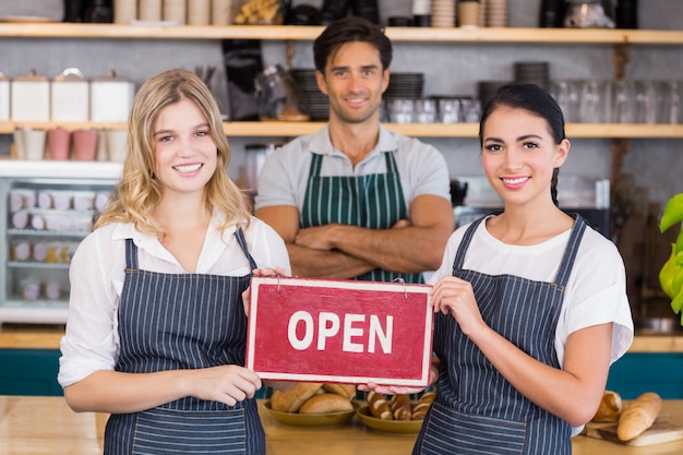 Smiling colleagues showing signboard with open sign