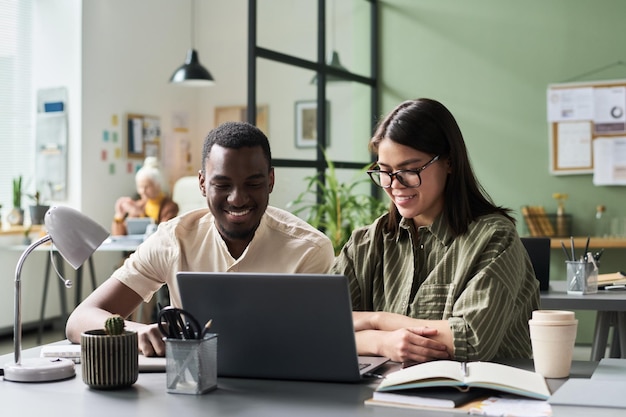 smiling colleagues working on laptop in modern office
